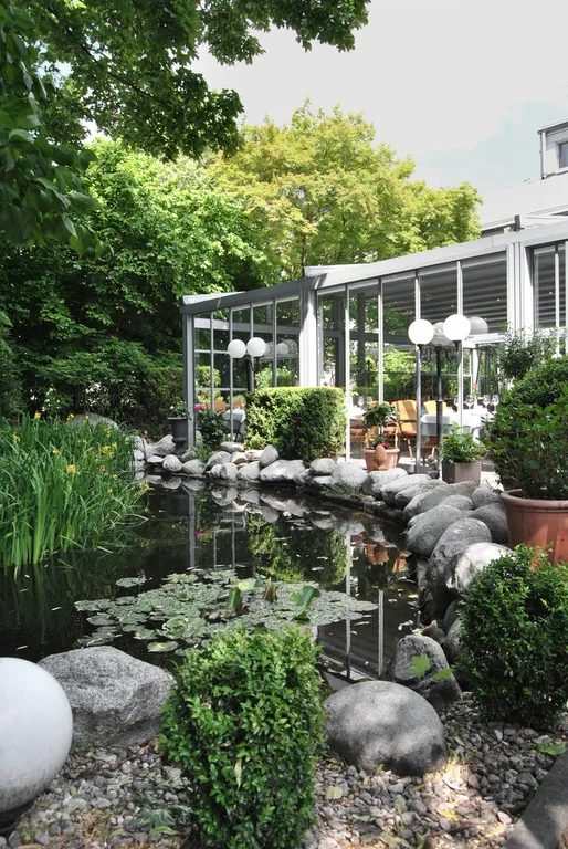 Begrünter Innenhof mit Teich und Glaswänden – der Cortile-Garten